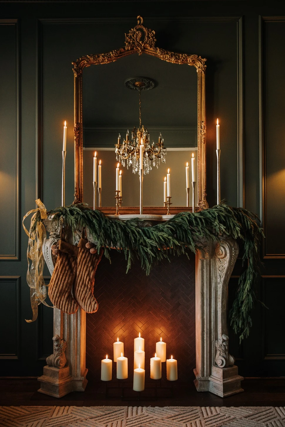 Full view of Victorian elegant faux fireplace with a large gold mirror on the mantle paired with candles and greenery.