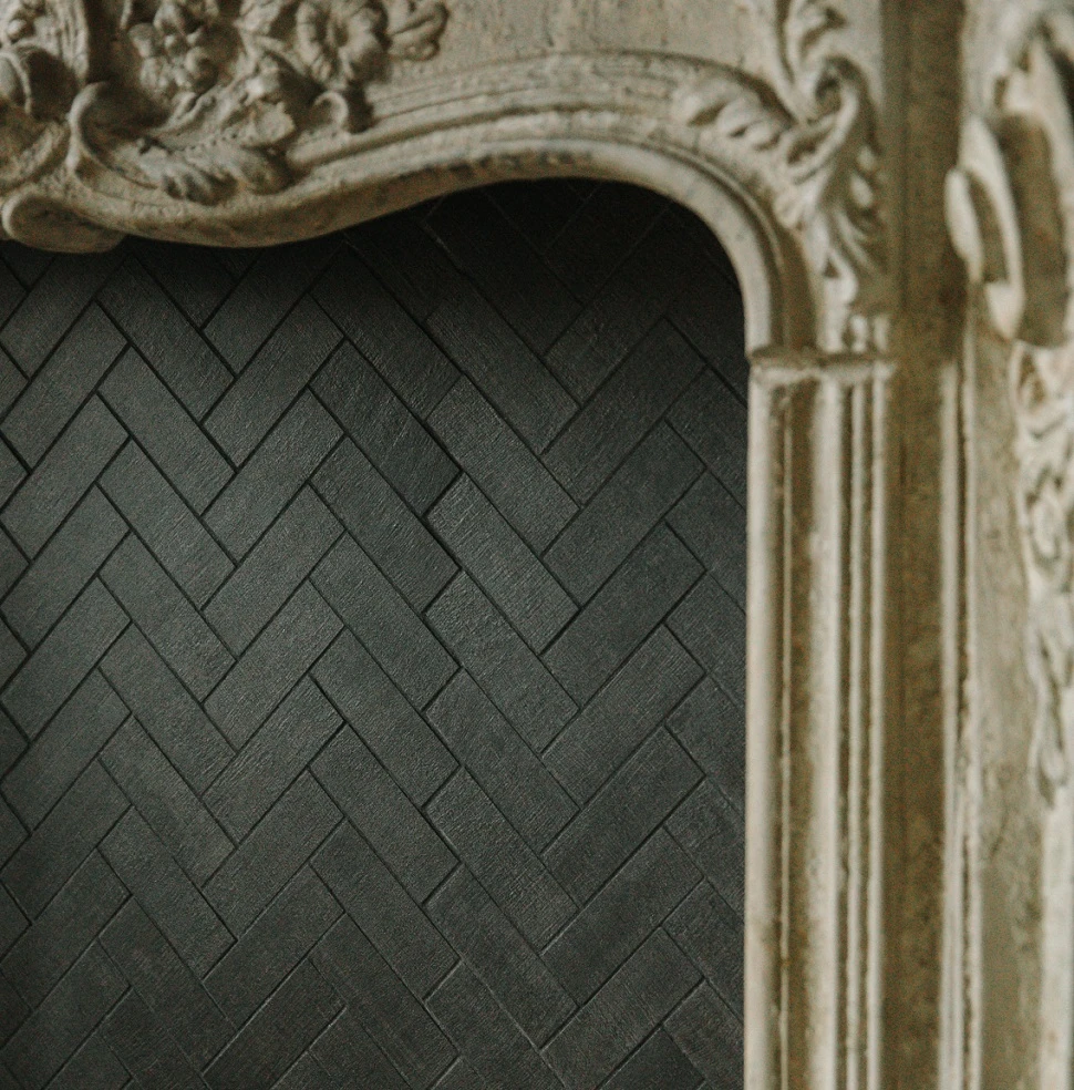 Close-up view of black fabric-look porcelain tiles completing the faux fireplace with greenery draped and gold candlesticks on the mantle.